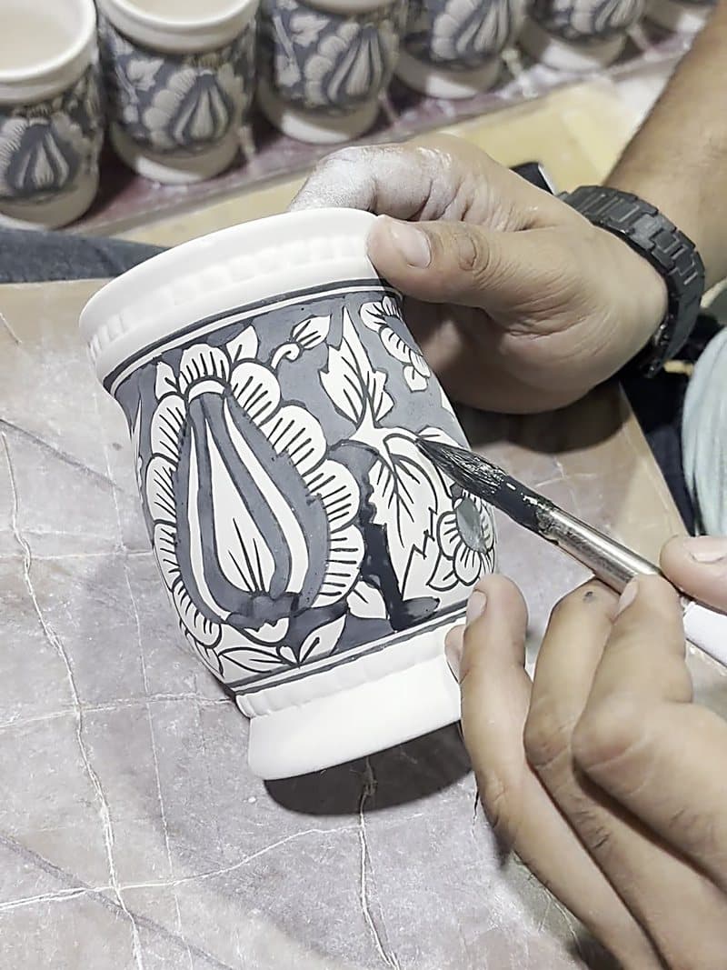 A ceramic jar being hand-painted with a fine brush before firing