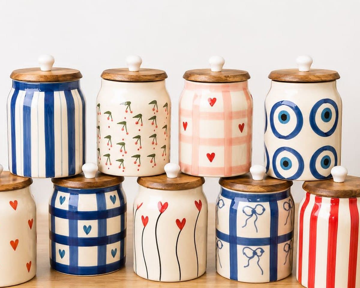 Nine hand-painted ceramic storage canisters with natural wood lids, in gingham, stripe, cherry, heart and evil eye prints