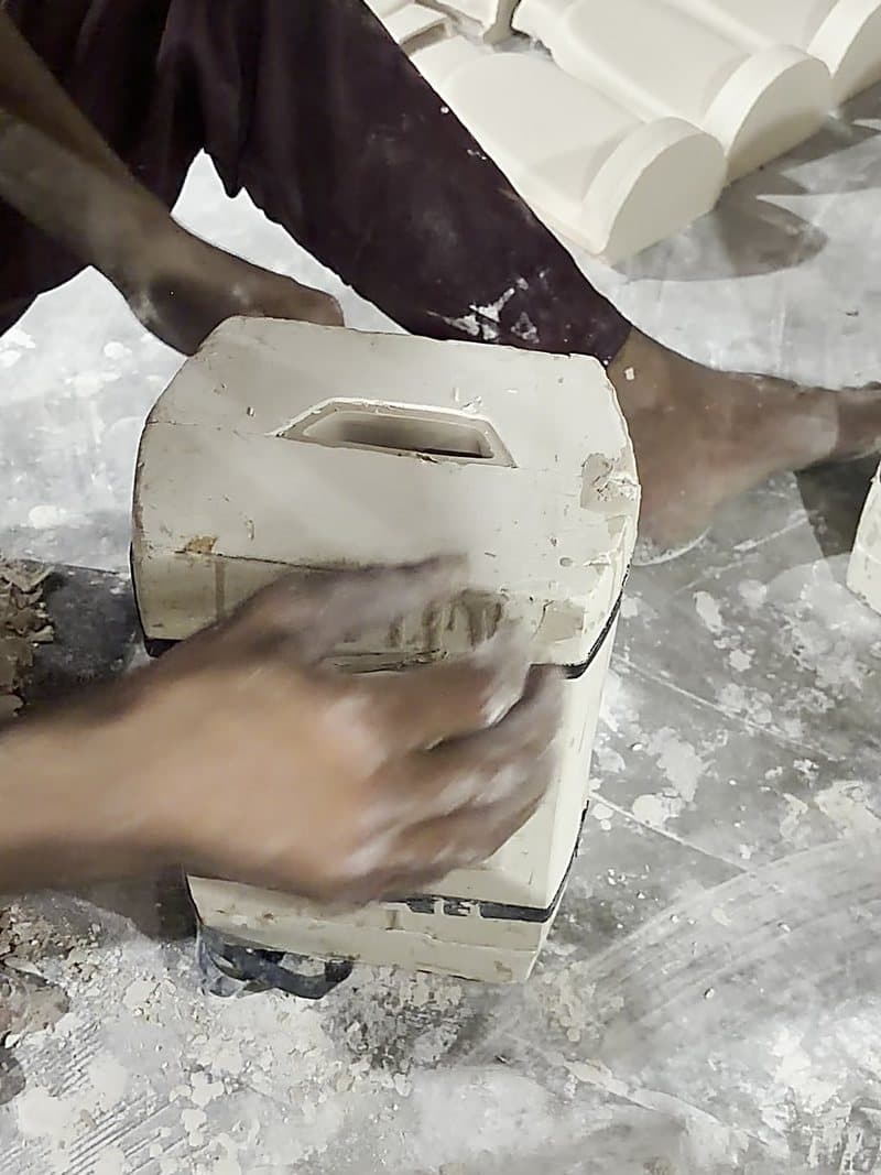 A cast ceramic piece being lifted out of its plaster mould by hand